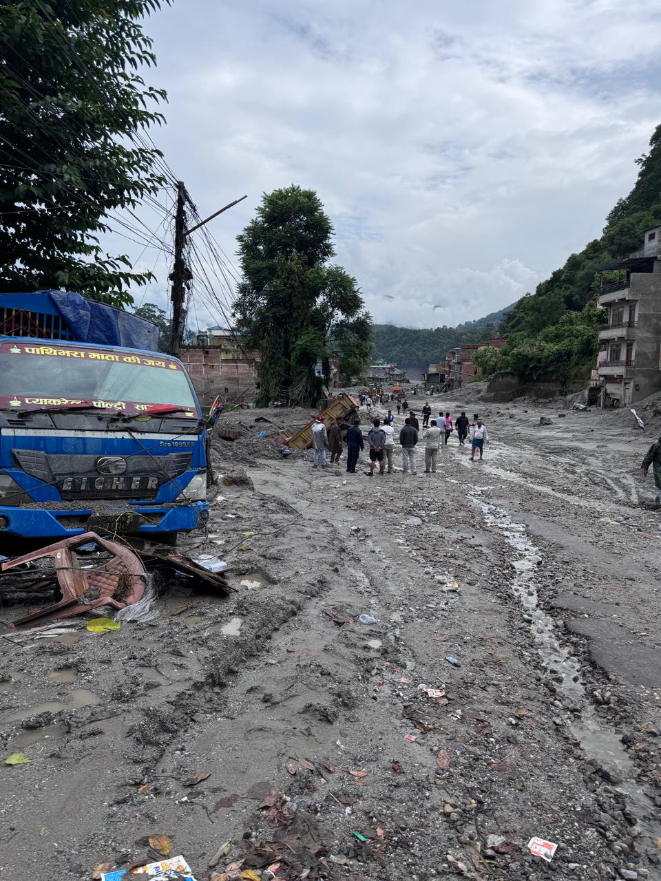 A supply truck on the debris-covered road as residents pass on foot.