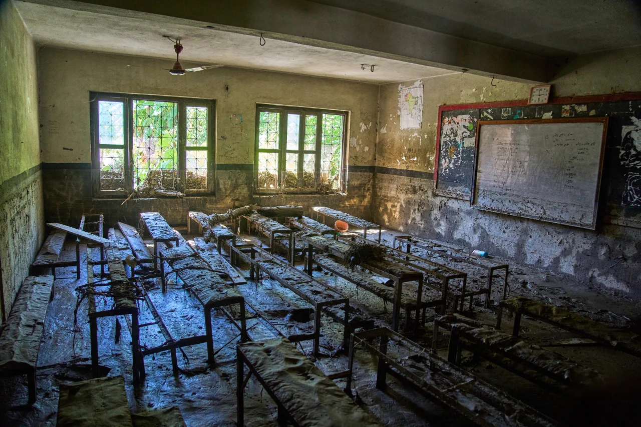 A classroom filled with flood silt, desks and benches caked in mud